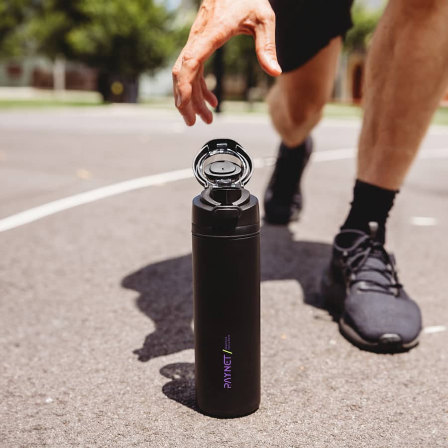 A drink bottle in black with a flip-top lid and a logo, positioned on a court beside a person in motion.