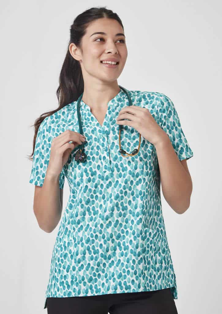 A turquoise tunic with a stardust print, featuring a collar and short sleeves, worn by a smiling woman holding a stethoscope.