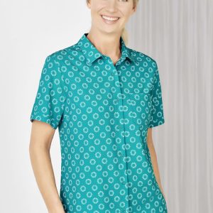 A short sleeve shirt in teal featuring a white daisy print and a button-up front. It has a single chest pocket.