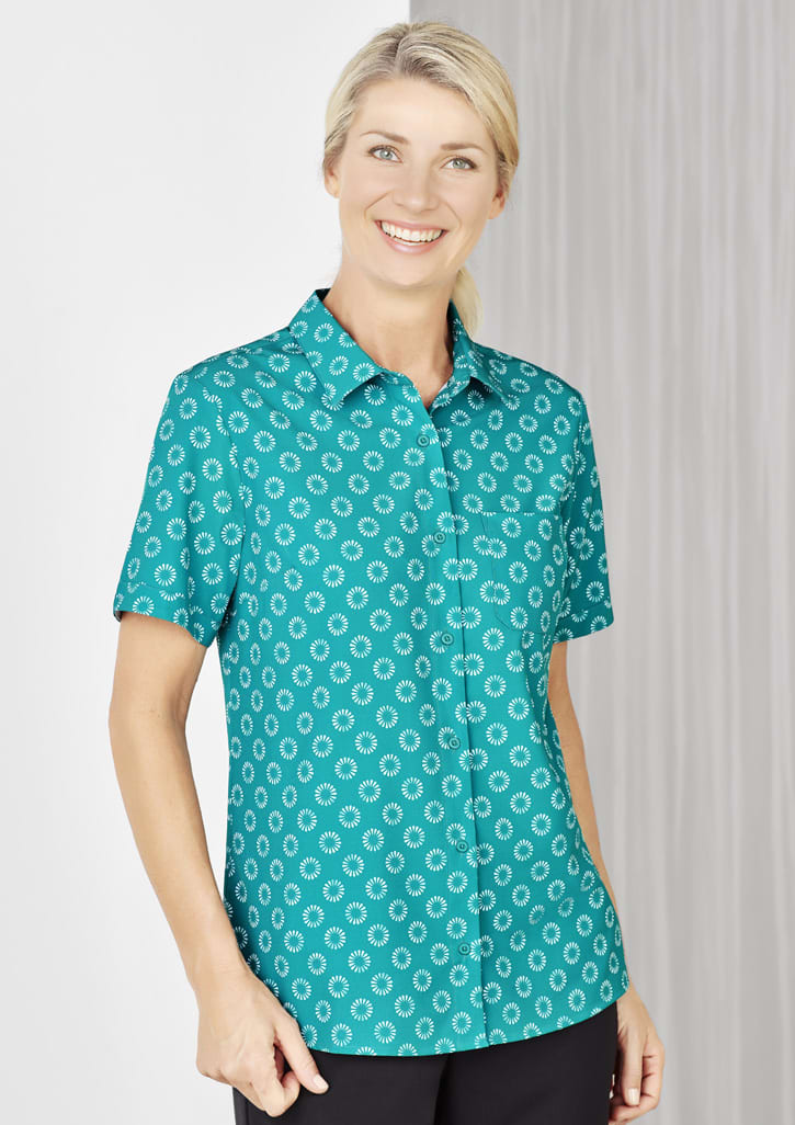 A short sleeve shirt in teal featuring a white daisy print and a button-up front. It has a single chest pocket.