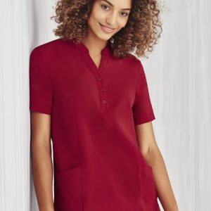 A burgundy women's tunic with a collar, short sleeves, buttons, and two front pockets. Features a logo.