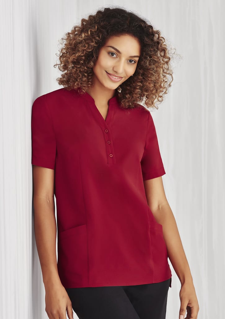 A burgundy women's tunic with a collar, short sleeves, buttons, and two front pockets. Features a logo.