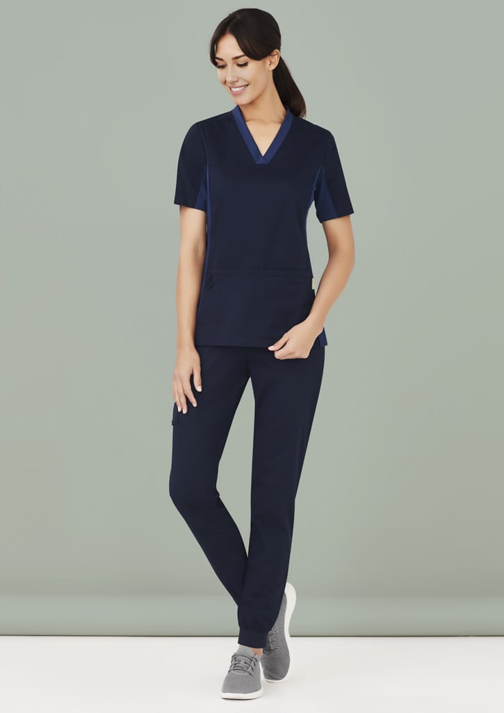 A woman wearing navy slim leg jogger scrub pants and a matching short-sleeve top, with a logo on the top.