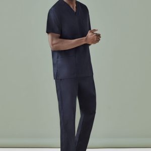 A man is wearing navy unisex scrub pants and a matching scrub top, standing against a plain green background.