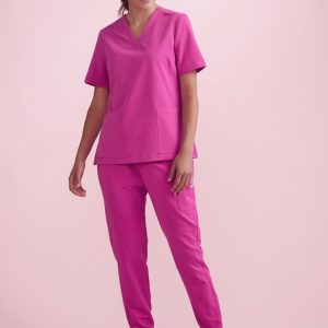 A model wearing women's pink jogger scrub pants and a matching pink scrub top, set against a light pink background.