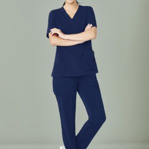 Navy blue women's scrub top and slim leg pant set, featuring pockets and a branding logo. Model is smiling.