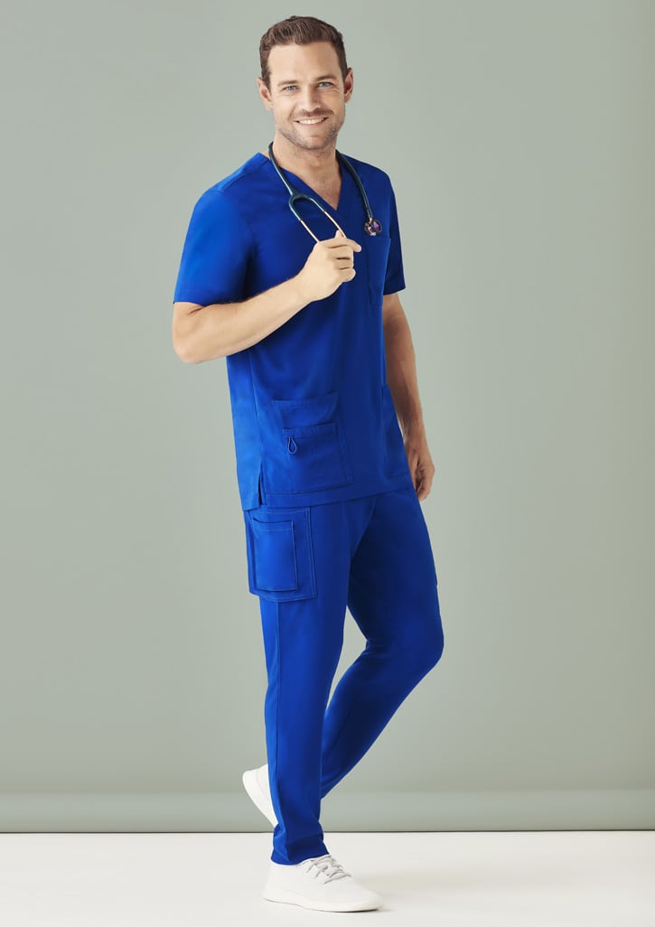 A man wearing royal blue scrub top and matching straight leg scrub pants, holding a stethoscope, against a light background.