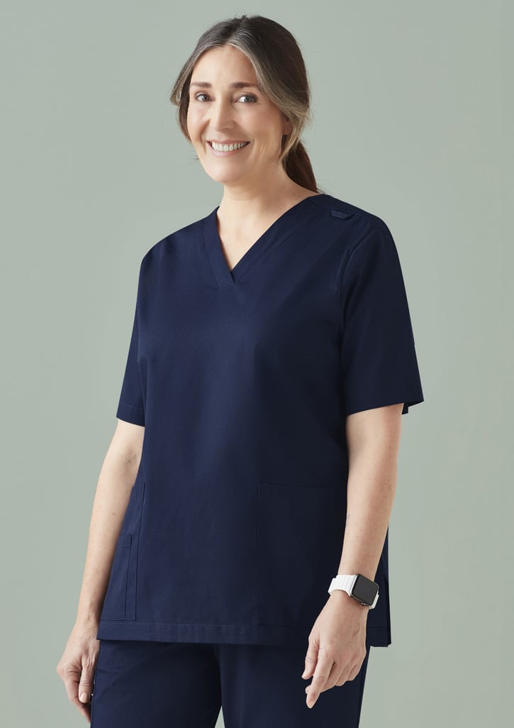A woman models a navy scrub top featuring a V-neck and side pockets, with a logo on the sleeve.