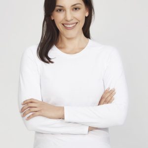 A white women's long sleeve performance tee, modelled by a smiling woman with arms crossed. The shirt has a logo.