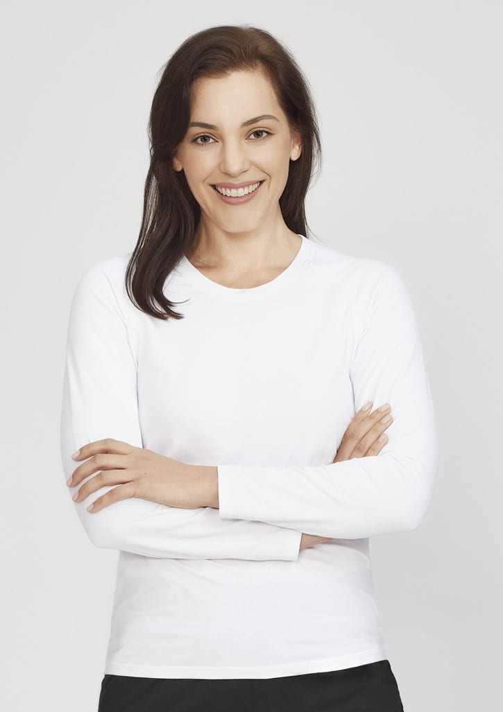A white women's long sleeve performance tee, modelled by a smiling woman with arms crossed. The shirt has a logo.