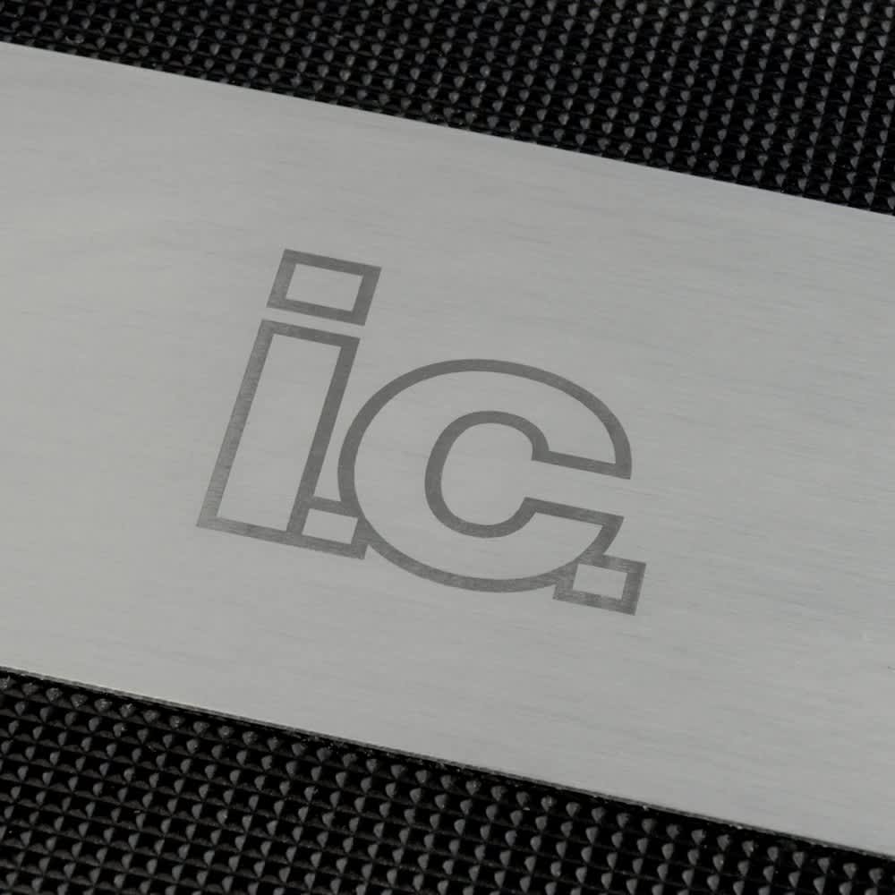 A stainless steel grilling spatula with engraved lettering on a textured black background.