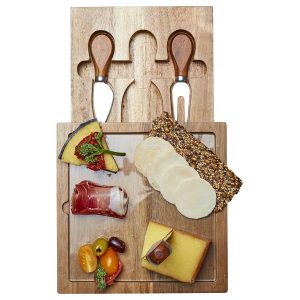 A wooden cheese board with assorted cheeses, meats, crackers, and two stainless steel cheese knives.