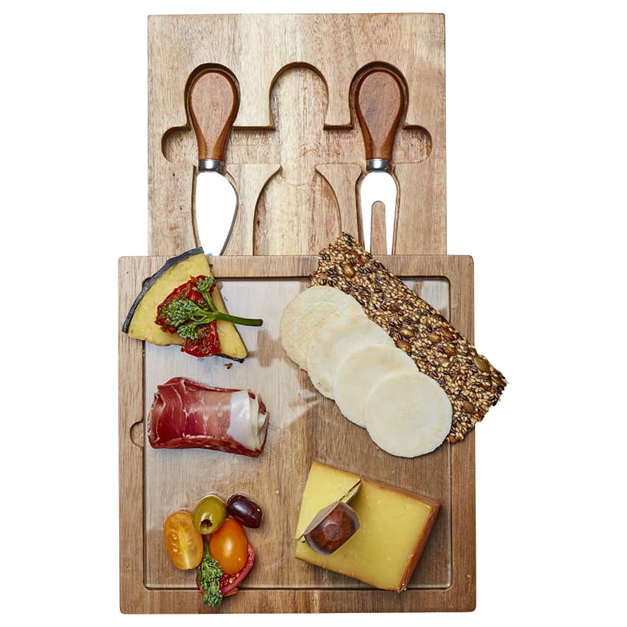 A wooden cheese board with assorted cheeses, meats, crackers, and two stainless steel cheese knives.