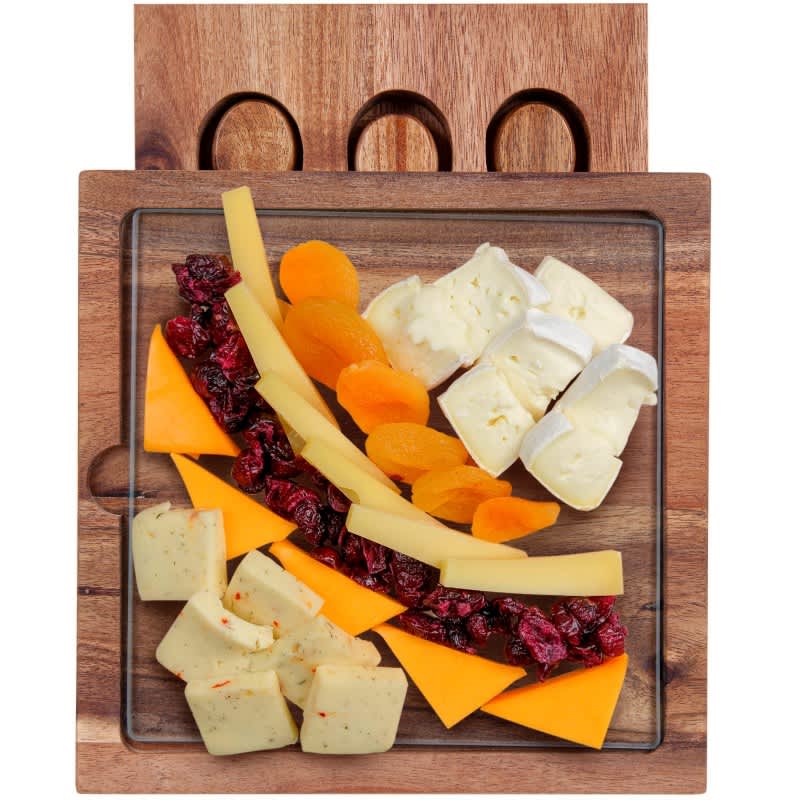 A glass cheese board with a wooden base, featuring assorted cheeses, dried fruits, and cranberries.