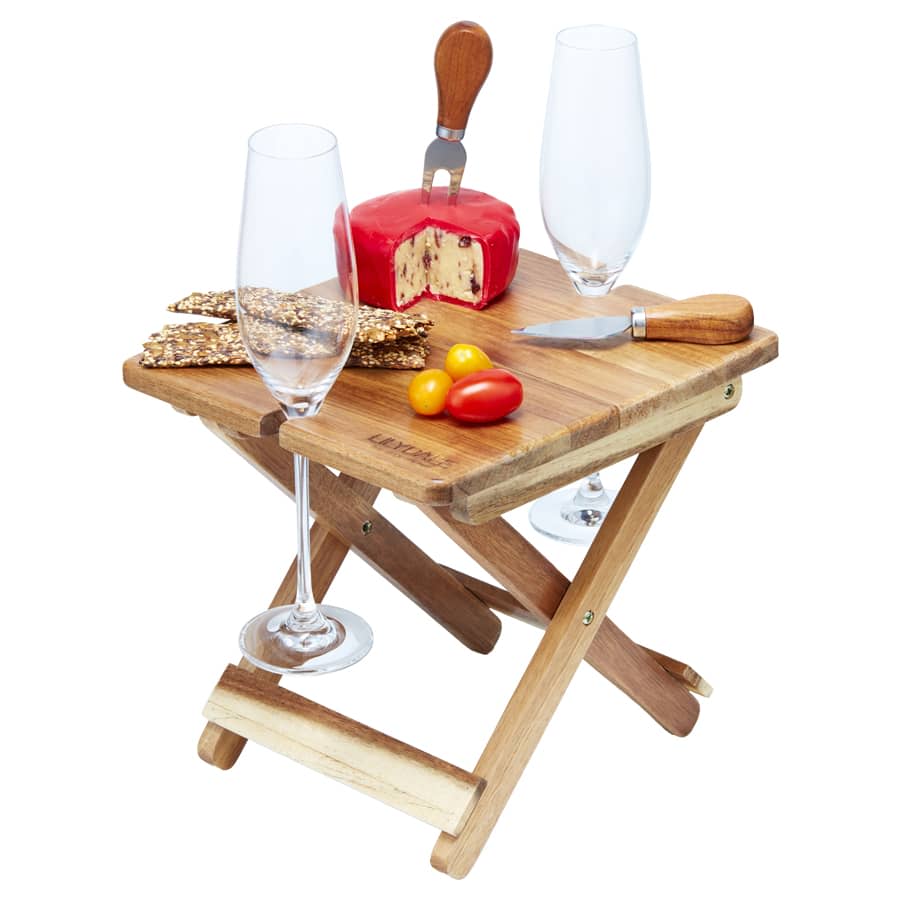 A foldable wooden cheese and wine board with a cheese block, knife, crackers, and two glasses.