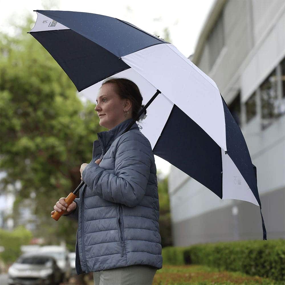 A golf umbrella featuring a navy and white design, held by a person wearing a grey jacket outdoors.