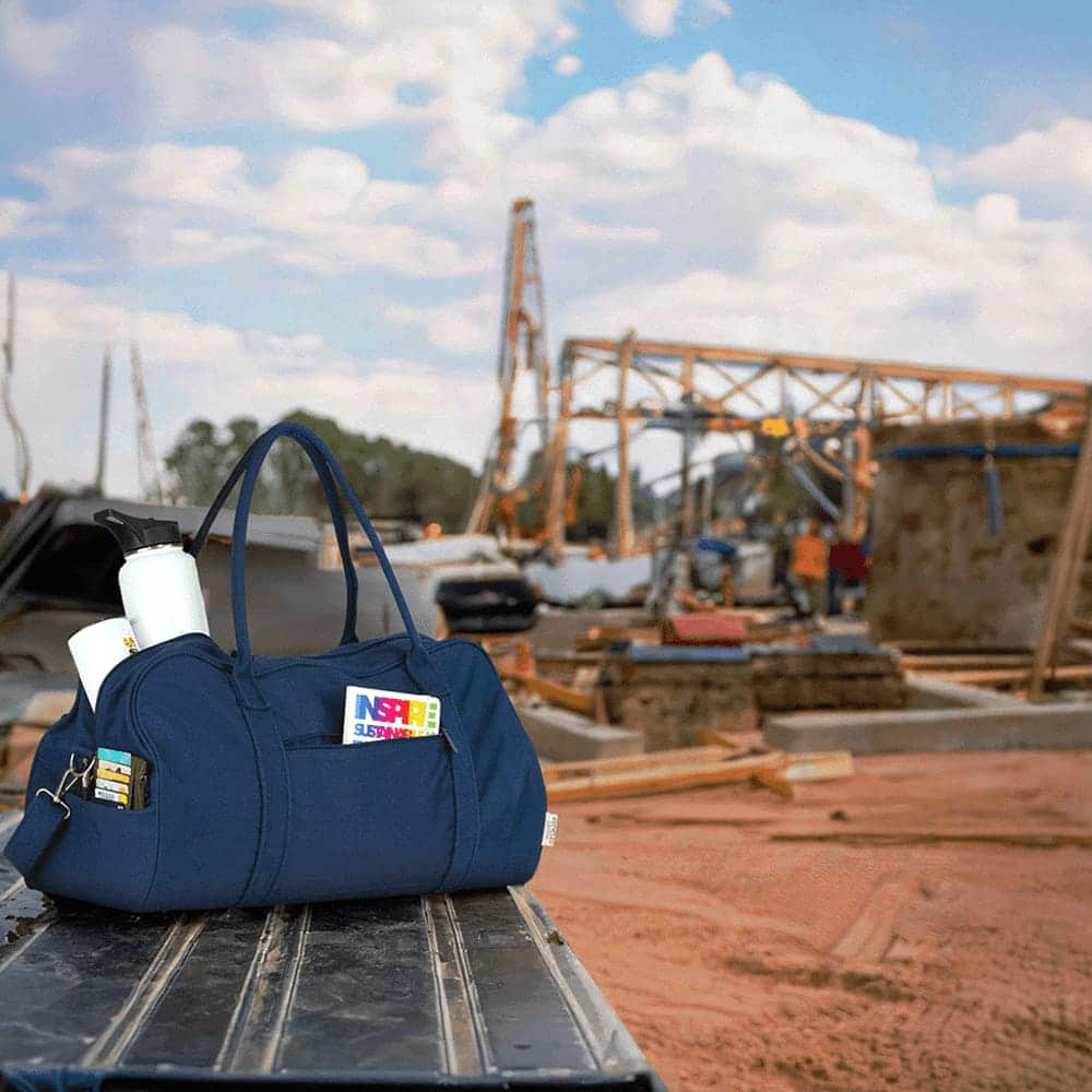 A navy duffel bag with a logo, featuring two handles and a detachable shoulder strap.