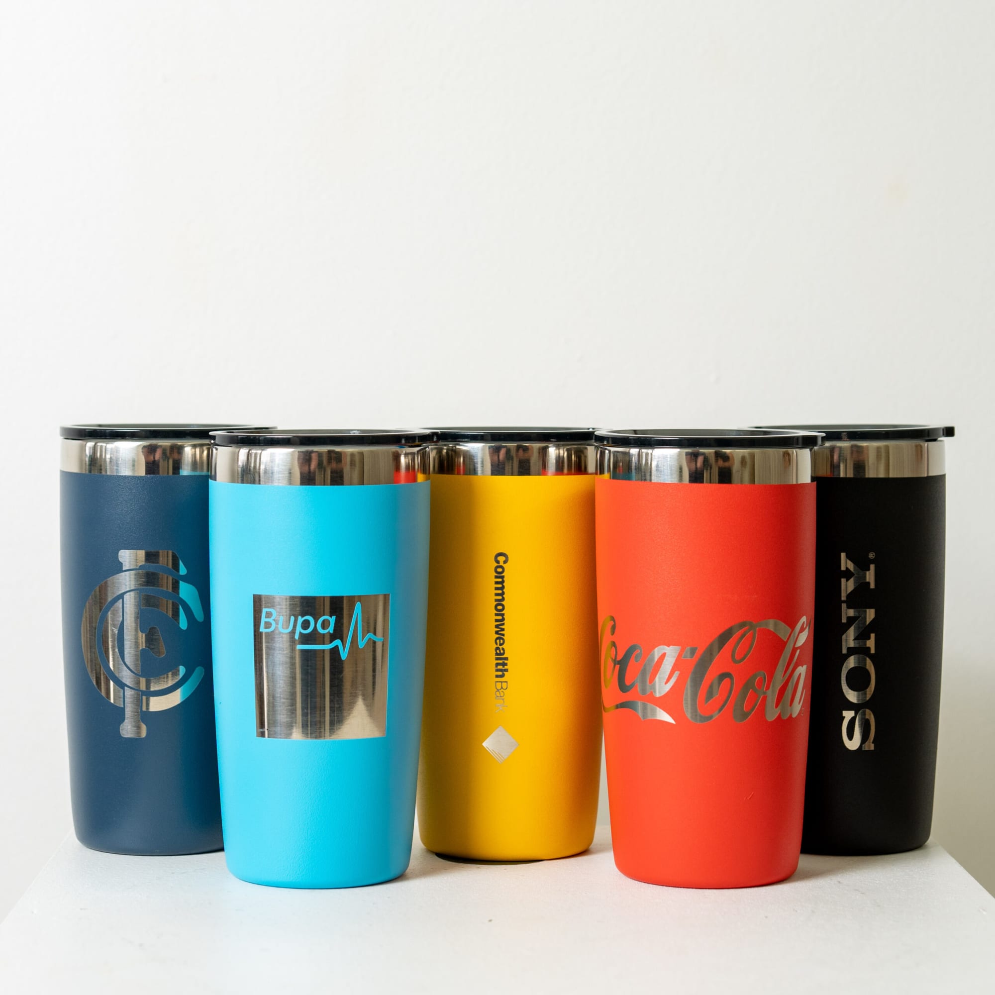 A drink tumbler set in various colours including navy, blue, yellow, red, and black, featuring logos on some.