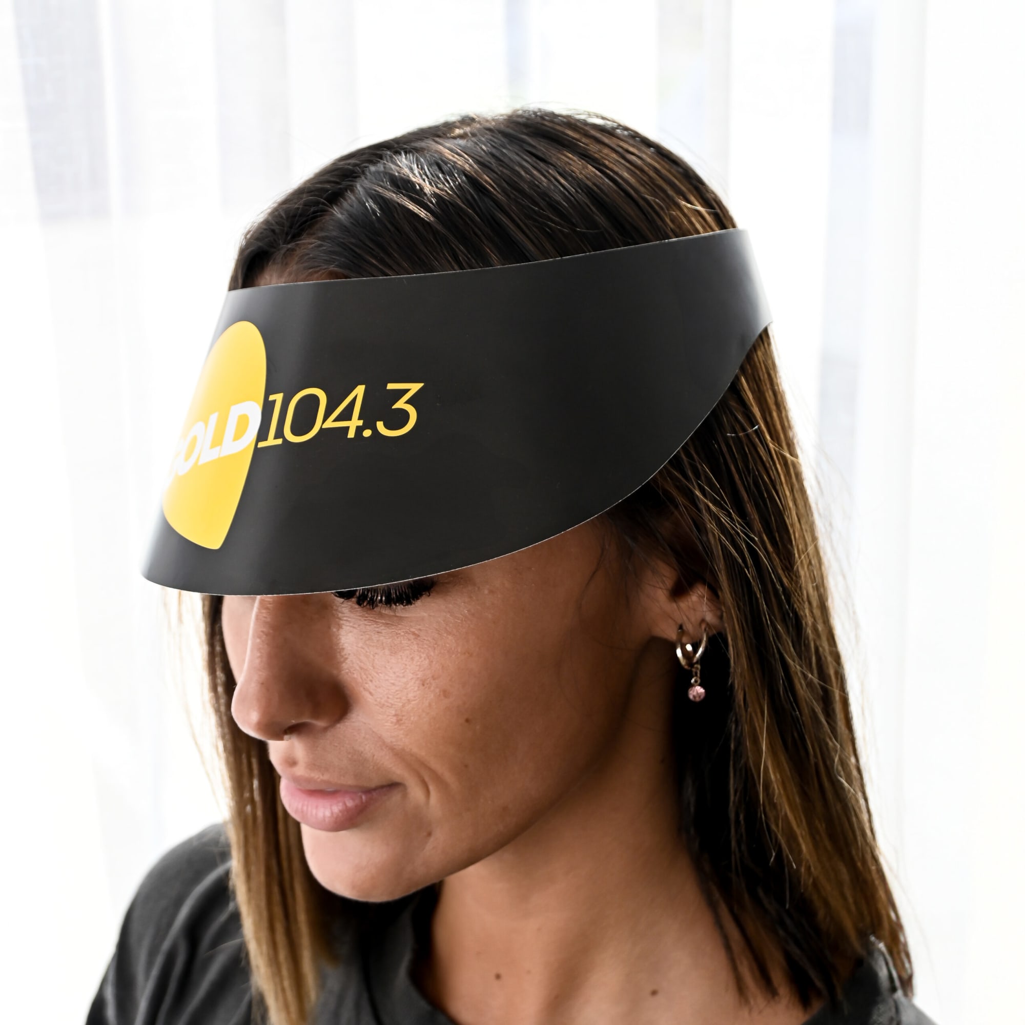 A black sun visor with a logo, worn by a woman with long hair, indoors against a light background.