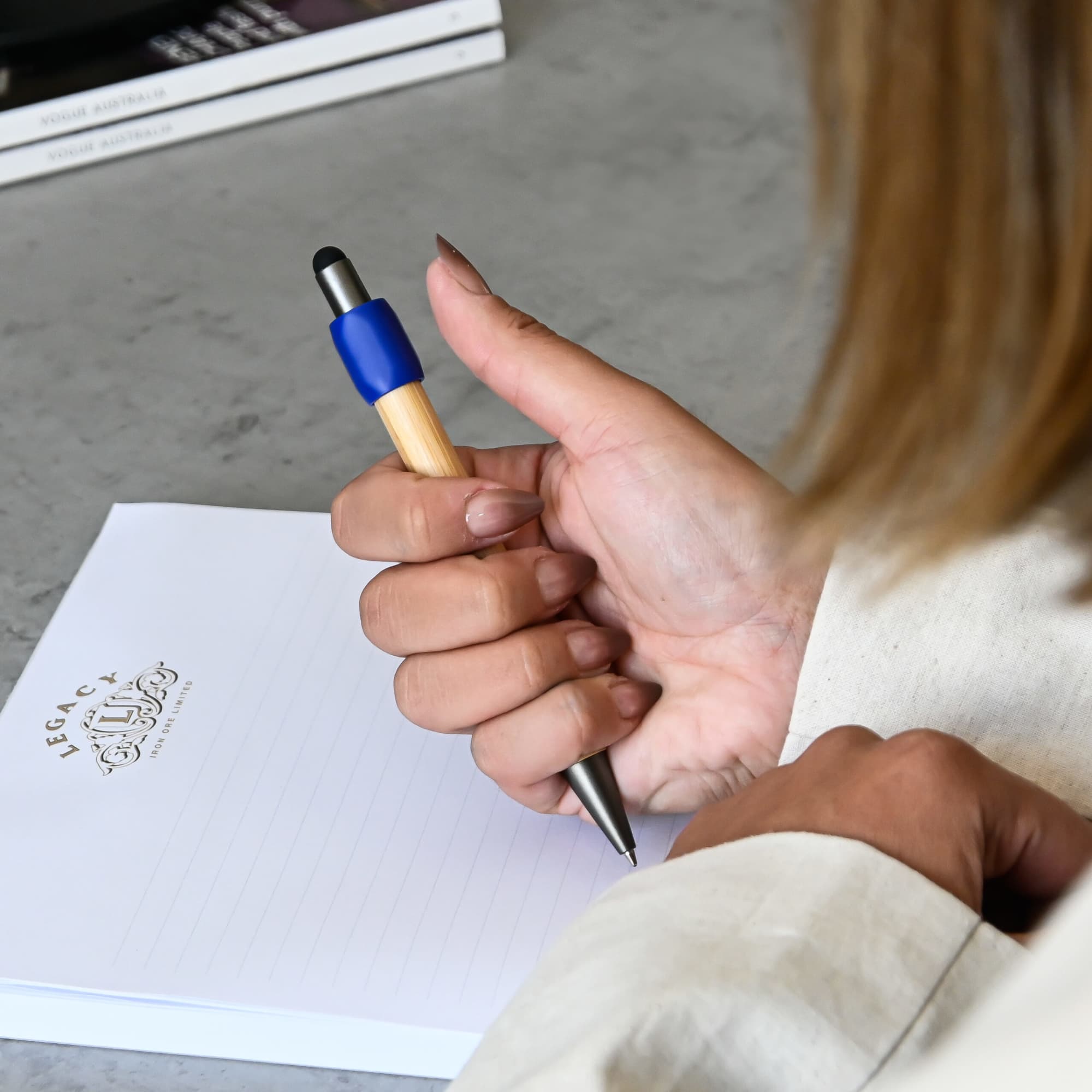 A bamboo spinner pen with a blue grip being held above a notepad on a grey surface.
