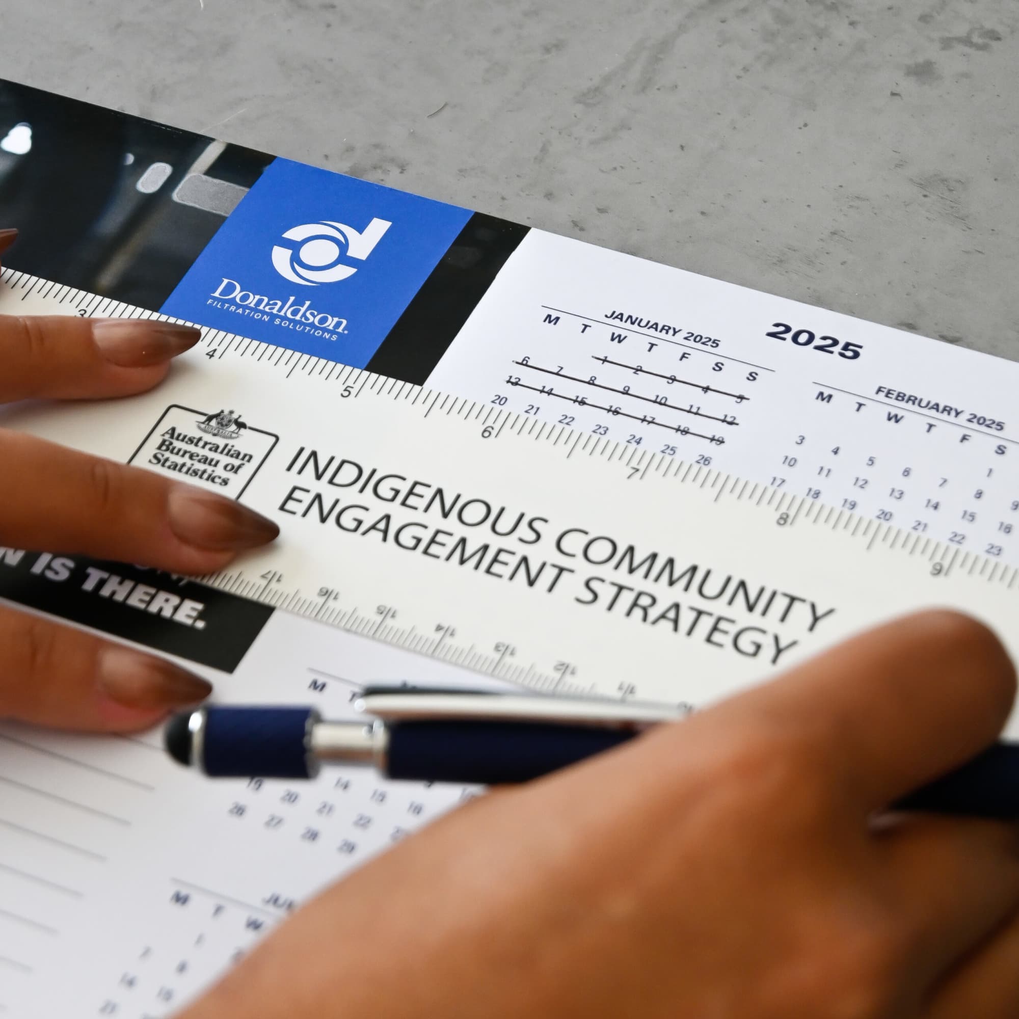 A ruler with a transparent edge and a logo, placed above a calendar and a document titled 