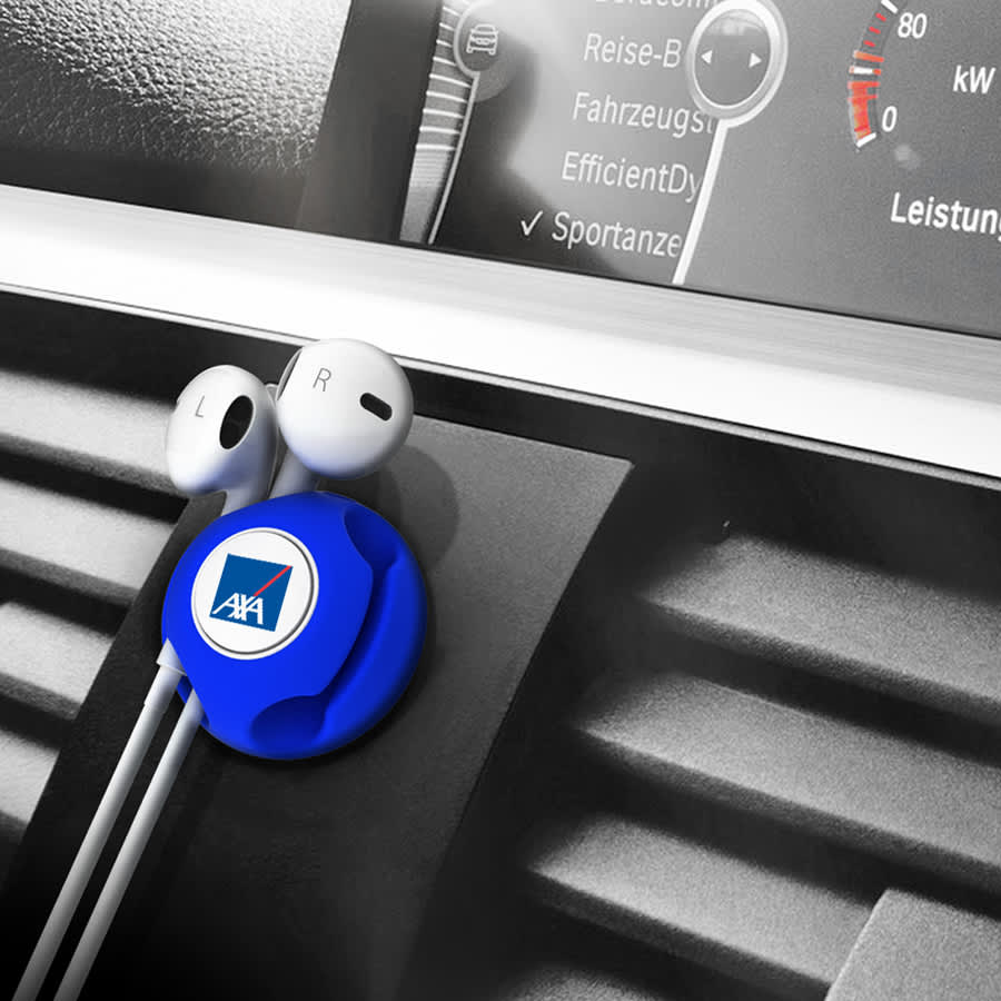 A blue cable manager with a logo, securing earphones on a car dashboard vent.