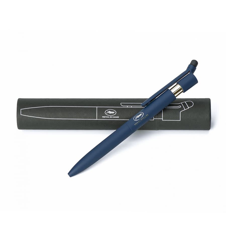 A blue metal ballpoint pen with a stylus, resting on a cylindrical black packaging, featuring a logo.