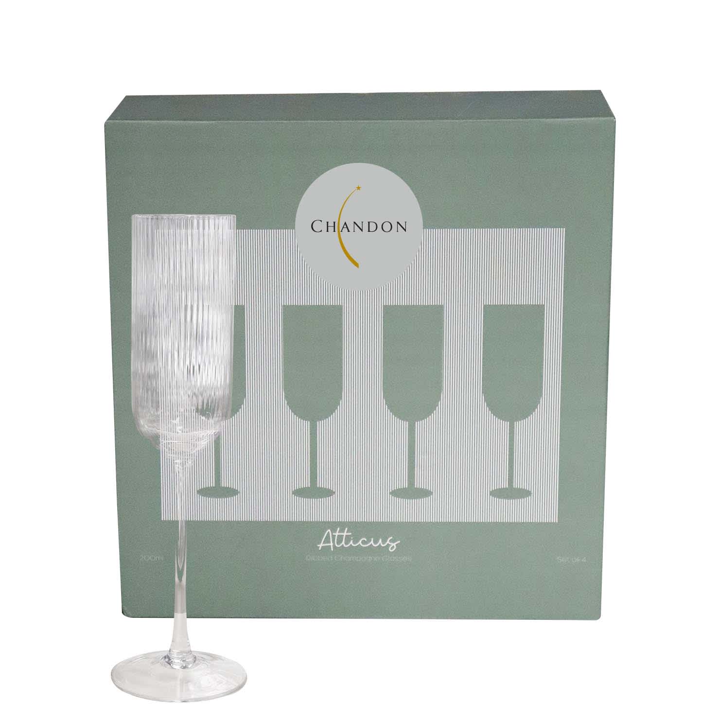 A clear glass champagne flute with a ribbed texture, displayed in front of its green packaging featuring an emblem.