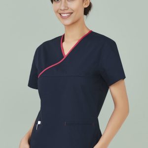 A navy scrub top with contrast red detailing, featuring a crossover design and pockets. The model is smiling.