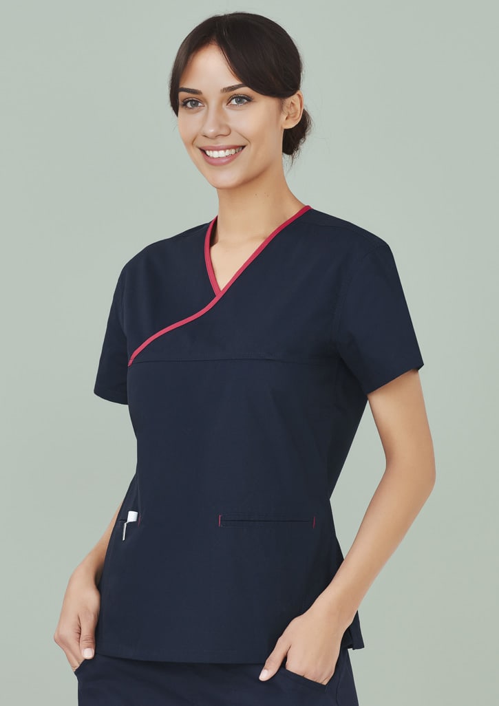 A navy scrub top with contrast red detailing, featuring a crossover design and pockets. The model is smiling.