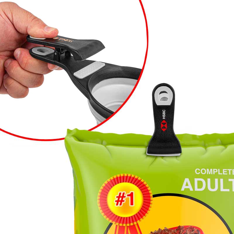A collapsible silicone pet food scoop in black and grey, with an integrated bag clip for storage.