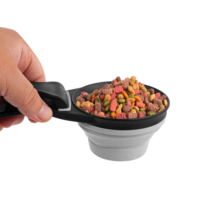 A collapsible silicone pet food scoop in black and grey, filled with colourful pet food, held in a hand.