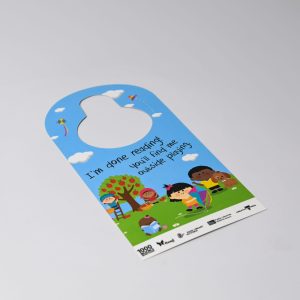 A door hanger featuring a colourful design with children playing outside, set against a blue background and greenery.