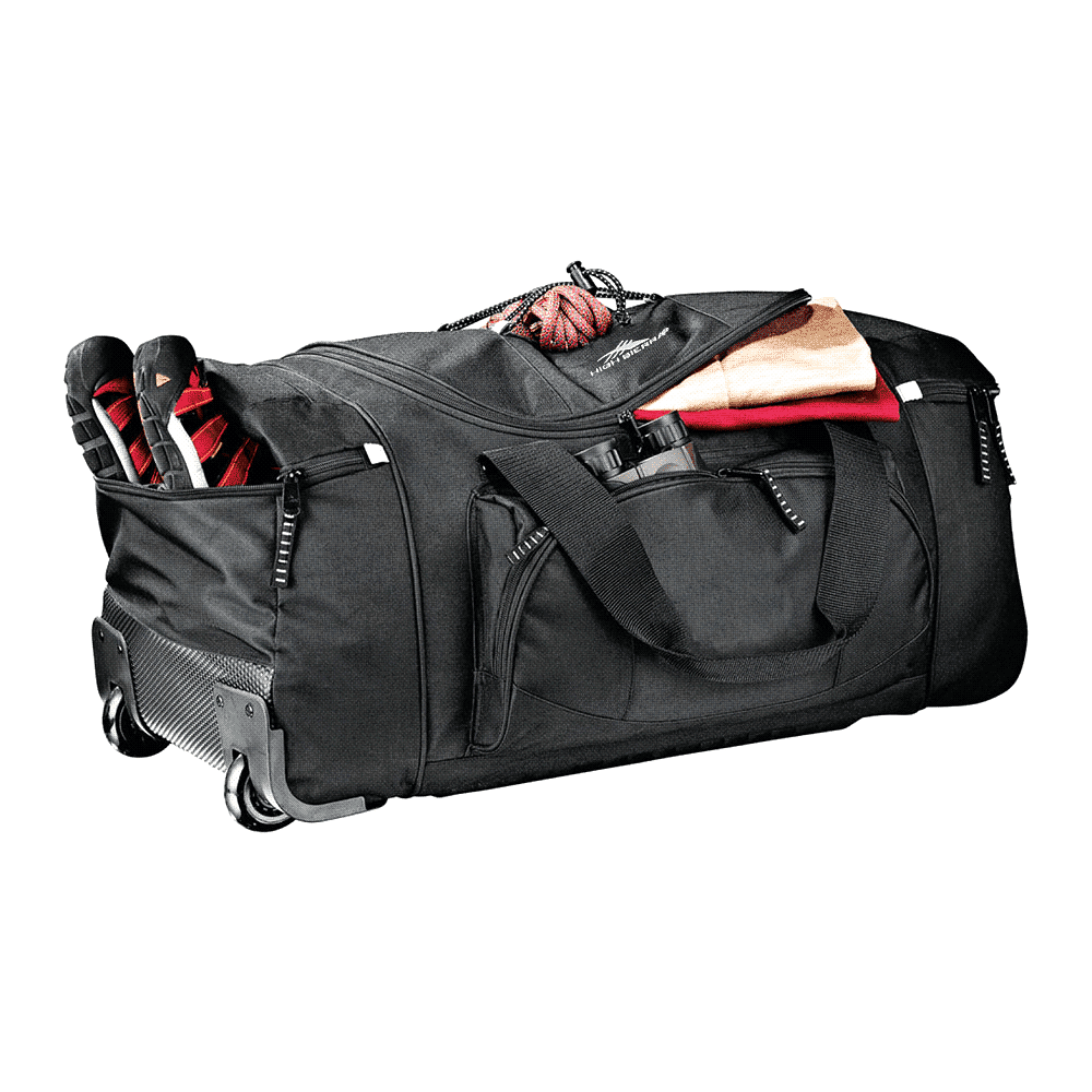 A wheeled duffel bag in black with multiple zippers, positioned on a dirt path against a blue sky.