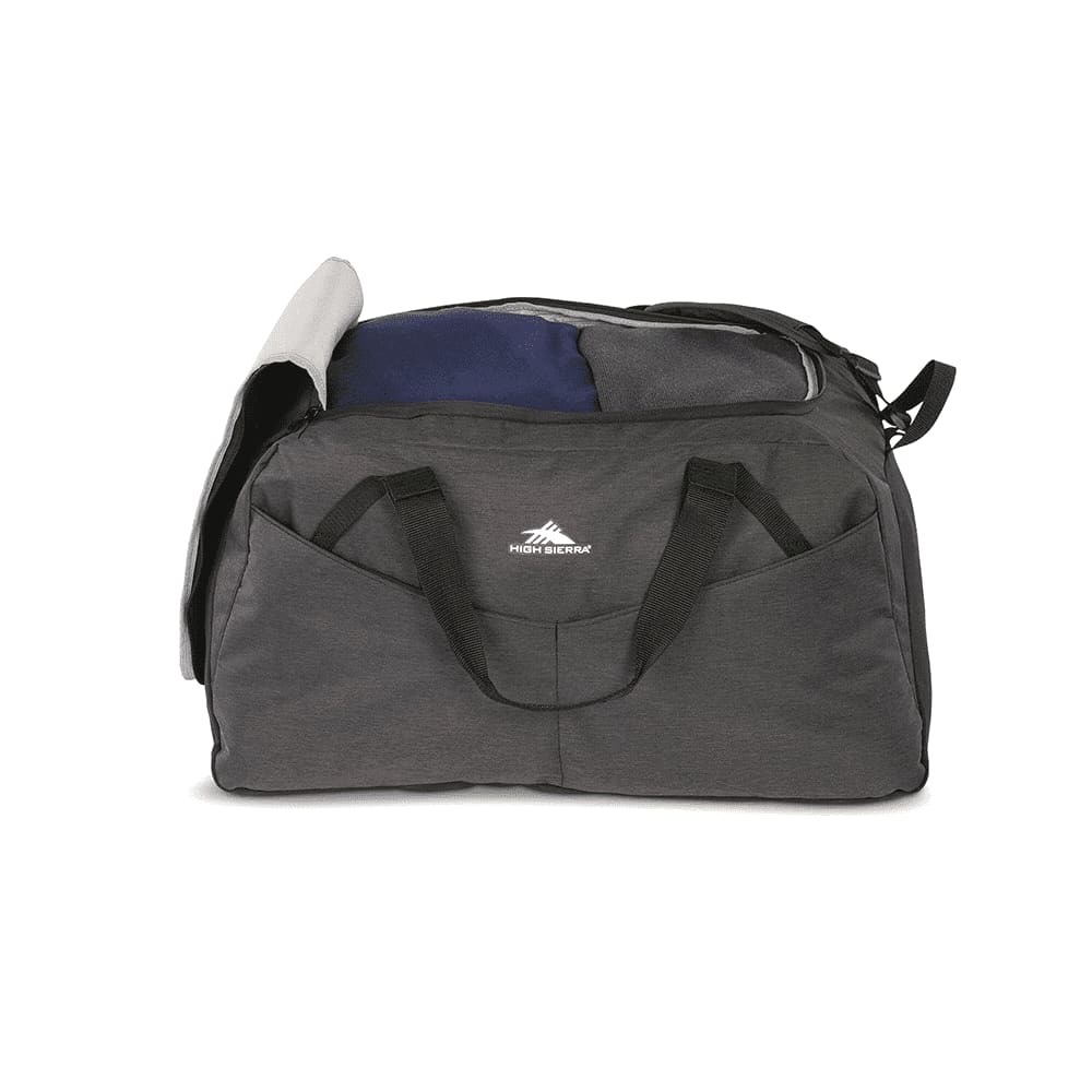 A man walks outdoors carrying a large grey duffel bag with black accents and a logo.