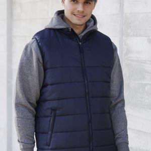 A man wearing a navy blue puffer vest over a grey hoodie, combined with denim jeans and a cap. The vest has a front zipper and pockets.