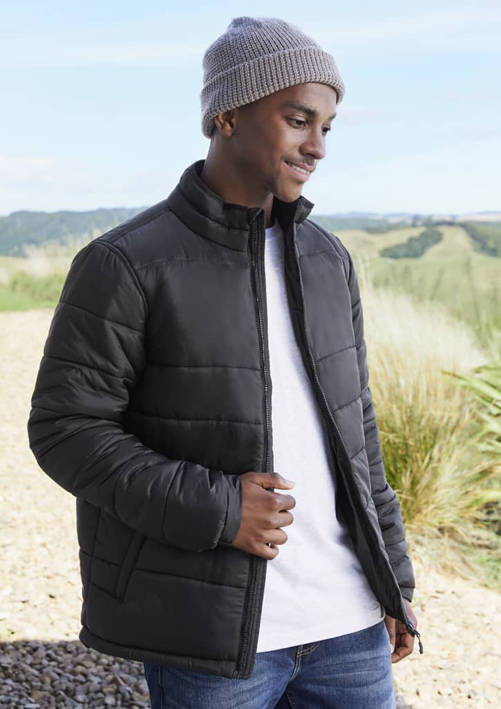A black puffer jacket with a zip, worn by a smiling man in a grey beanie, set against a scenic outdoor background.