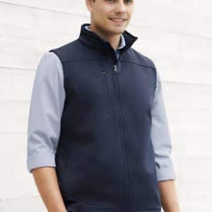 A navy softshell vest with a zip front, worn over a light blue shirt, includes a branding logo.