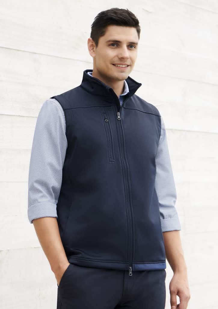 A navy softshell vest with a zip front, worn over a light blue shirt, includes a branding logo.