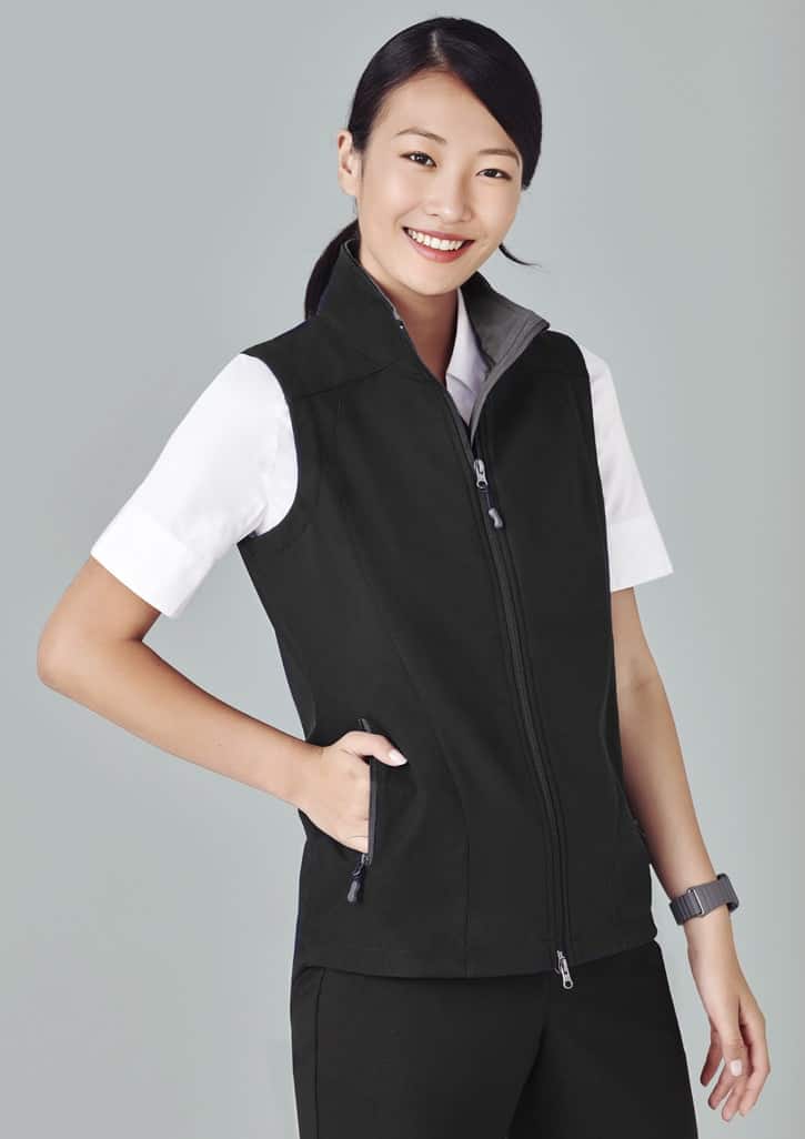 A black women's vest with a zip front, featuring a grey collar and side pockets, worn over a white shirt.