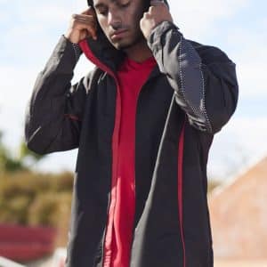 A unisex jacket in black with red accents, featuring a hood and lightweight design, displayed by a model.