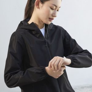 A black women's rain jacket with a hood, featuring elastic cuffs and a zippered front, displayed by a model.
