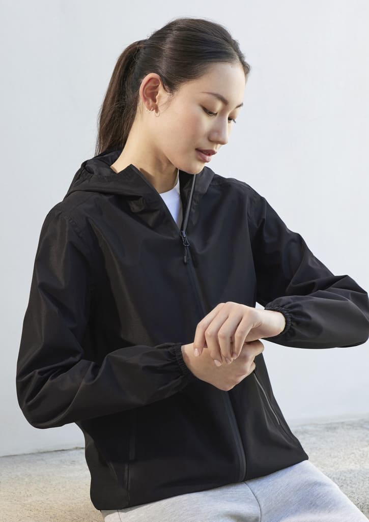A black women's rain jacket with a hood, featuring elastic cuffs and a zippered front, displayed by a model.