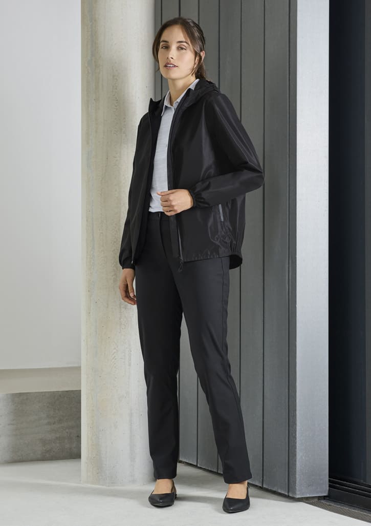 A women's black rain jacket with a hood, paired with black trousers and a white shirt. The model stands against a modern backdrop.