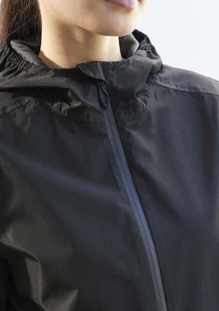 A black rain jacket featuring a hood and a zipped front, worn by a model. The jacket also has a logo.