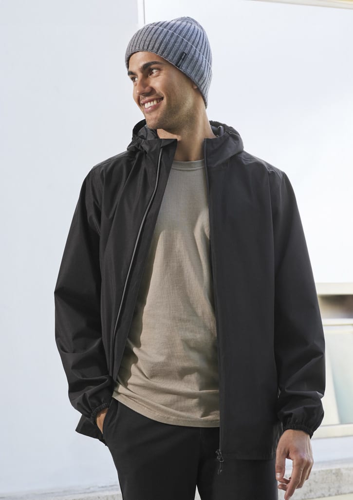 A man wearing a black rain jacket and a grey beanie, smiling while standing outdoors.