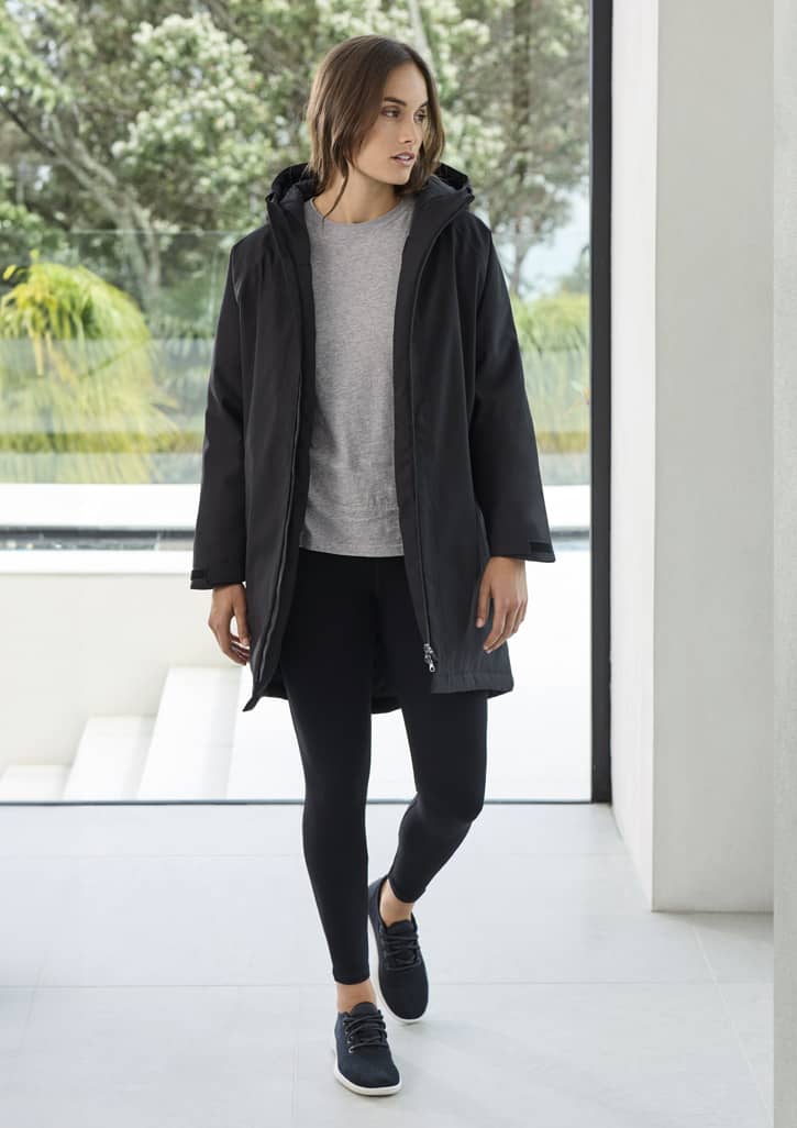 A unisex black rain jacket is worn by a model, paired with a grey top and leggings, in a modern indoor setting.