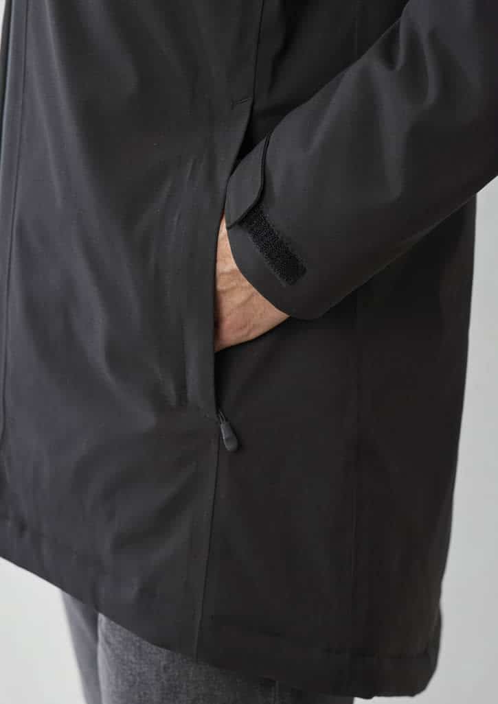 A close-up of a black unisex rain jacket showing a hand in the pocket and sleeve details with a fastening.
