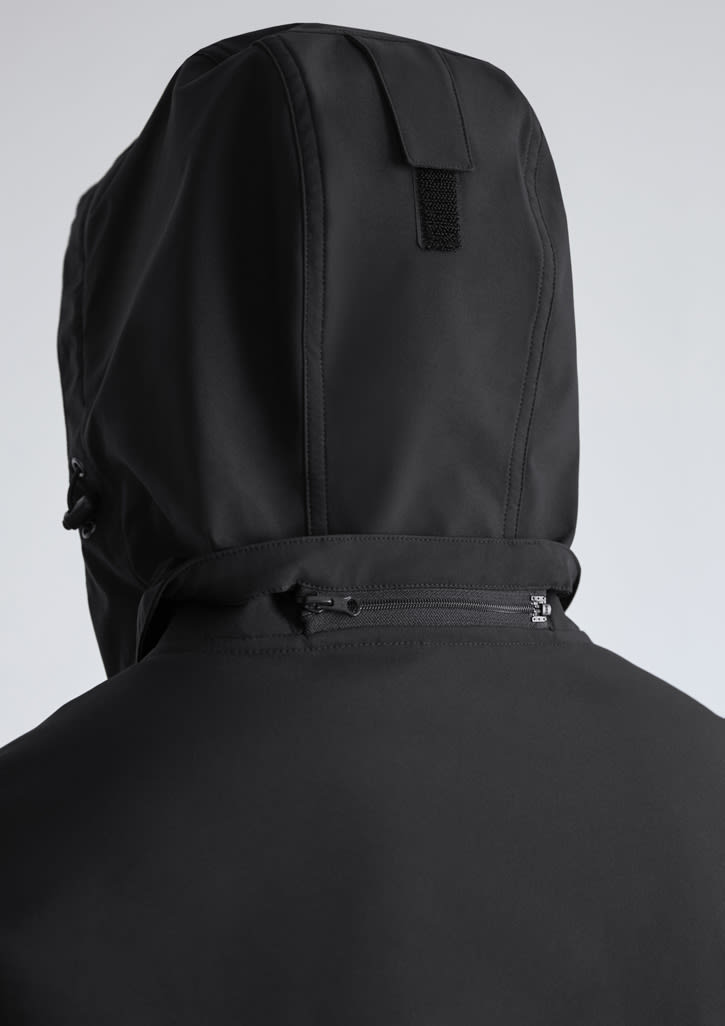 A black women's jacket with a hood, featuring a zippered pocket and a textured fabric design.