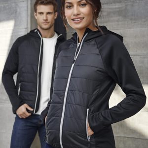 A woman models a black puffer jacket with a zip, featuring a hood and contrasting details. A man stands behind her in a white shirt.